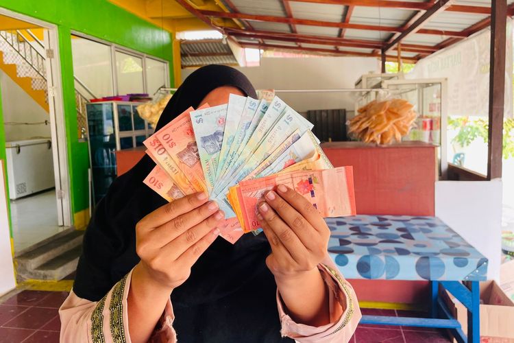 Seorang pemilik rumah makan di Entikong, Kabupaten Sanggau, Kalimantan Barat, menunjukkan uang ringgit Malaysia yang dia terima dari pelanggannya, Kamis (17/8/2023).