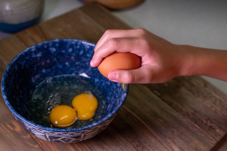 Ilustrasi memecahkan telur dengan mengetuknya ke pinggir mangkuk.