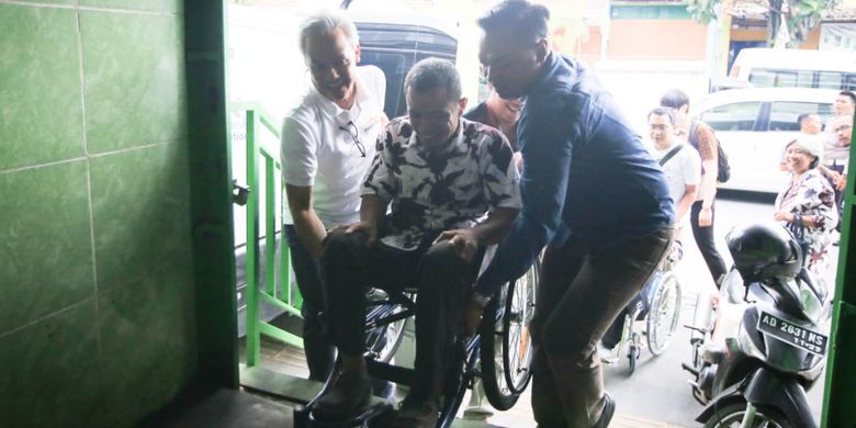 Gubernur Jawa Tengah Ganjar mengangkat kursi roda dari penyandang disabilitas saat memasuki rumah makan di Solo, Jawa Tengah, Sabtu (23/2/2019).