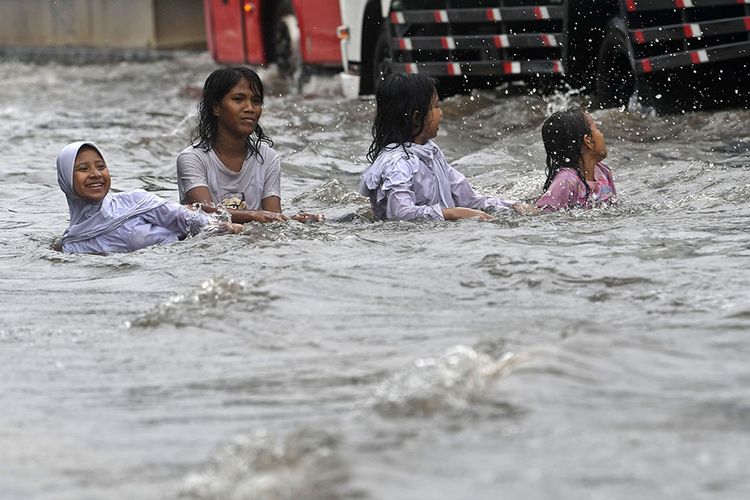 Sejumlah anak bermain air yang membanjiri Jalan Gunung Sahari di Pademangan, Jakarta, Jumat (24/1/2020). Hujan yang mengguyur sejak Jumat pagi hingga siang hari tersebut memicu banjir setinggi 30-50 centimeter di jalan raya itu sehingga menyebabkan lalu lintas kendaraan bermotor dan roda perekonomian warga setempat tersendat.