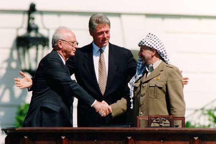 PM Israel Yitzak Rabin berjabat tangan dengan pemimpin PLO Yasser Arafat disaksikan Presiden AS Bill Clinton usai penandatanganan Perjanjian Oslo di Washington DC pada 13 September 1993.
