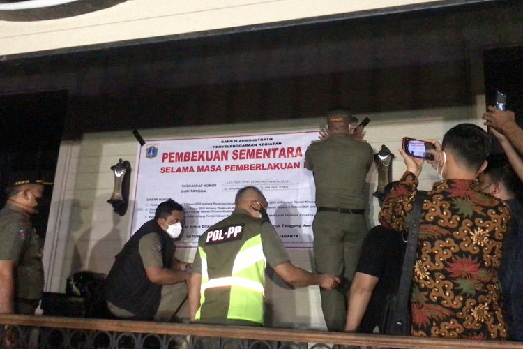 Satpol PP DKI Jakarta memasang spanduk tanda pembekuan operasional Holywings Cafe imbas dari pelanggaran jam operasional dan protokol kesehatan pada Senin (6/9/2021) malam.