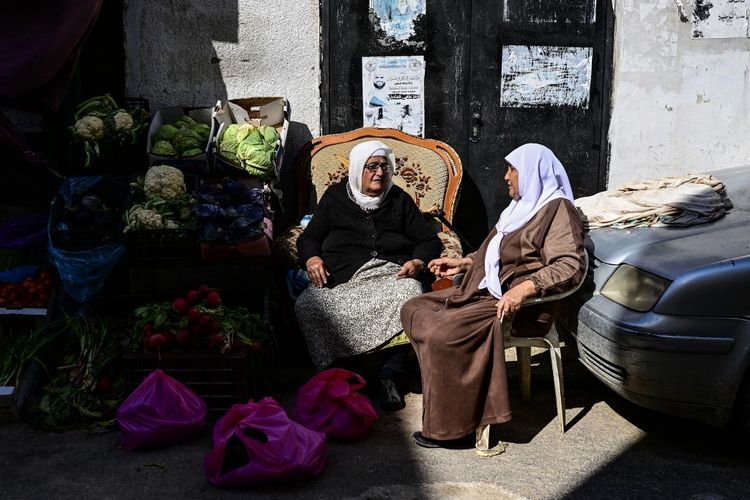 Sebuah foto yang diambil pada tanggal 20 Maret 2024, menunjukkan seorang perempuan Palestina yang menjual sayuran di sebuah warung pinggir jalan mengobrol dengan seorang pelanggan selama bulan suci Ramadhan di kamp pengungsi Jenin di Tepi Barat yang diduduki. 