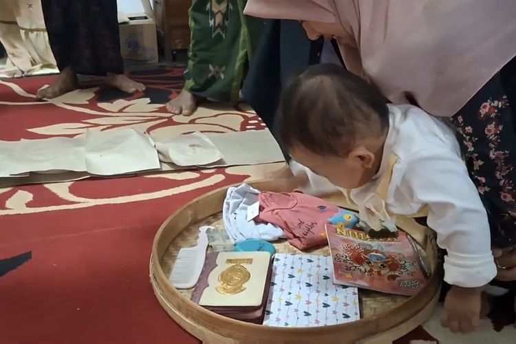 Anak Taufik Hidayat dituntun memilih barang yang berada di anyaman tampah dalam prosesi Tedak Siten, sebagai simbol doa untuk masa depan anak.