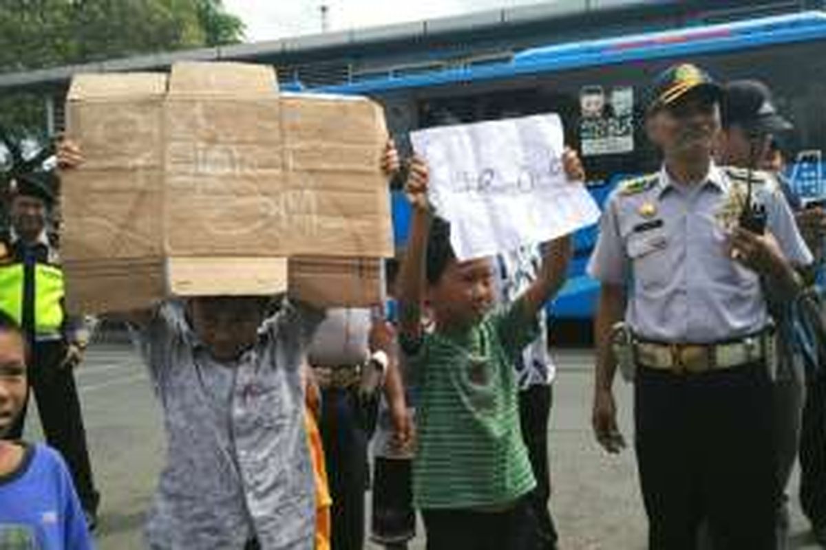 Anak-anak menunjukkan kertas dan kardus bertuliskan 