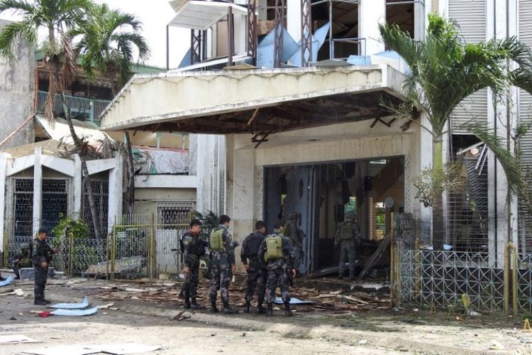 Polisi dan tentara berdiri di luar gereja yang terkena bom di Jolo, provinsi Sulu di pulau selatan Mindanao, Filipina, Minggu (27/1/2019). (AFP/NICKEE BUTLANGAN).