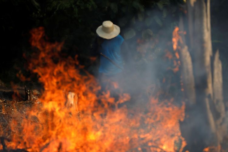 Seorang pria bekerja di tengah api yang berkobar di Amazon. Hutan hujan tropis terbesar dunia itu mengalami kebakaran terparah pada tahun ini.