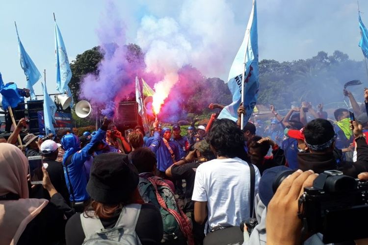 Polisi menghentikan asap flare yang menyala dari kerumunan peserta Hari BuruhKonfederasi Serikat Pekerja Seluruh Indonesia (KSPSI) di depan Monas, Jakarta Pusat pada Selasa (1/5/2018). 