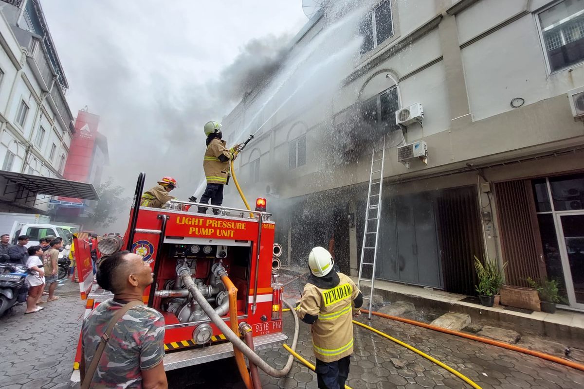 Pemadam kebakaran berupaya memadamkan api yang membakar ruko di Jalan Ruko Permata, Pademangan, Jakarta Utara pada Senin (26/12/2022). Kepulan asap hitam tampak membubung dari titik kebakaran. 