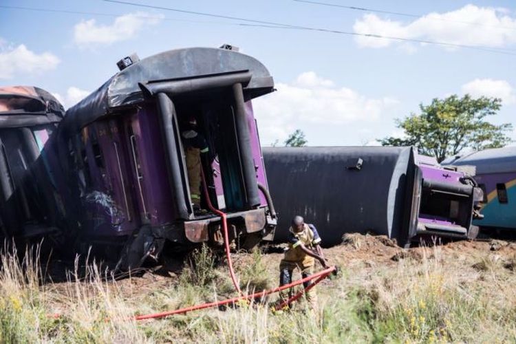 Seorang petugas pemadam kebakaran menarik selang di samping gerbong kereta terguling, setelah terjadi kecelakaan di dekat Kroonstad di provinsi Free State, Afrika Selatan, Kamis (4/1/2018). (AFP via VOA)
