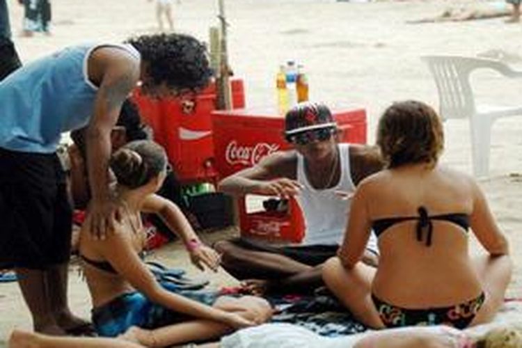 Two local beach boys chat with women tourists on Kuta beach in the tourism resort island of Bali