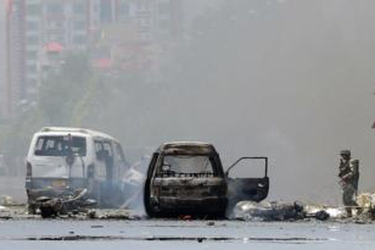 Seorang anggota pasukan keamanan Afganistan berdiri di dekat bangkai mobil yang terbakar akibat baku tembak di dekat gedung parlemen di ibu kota Kabul, Senin (22/6/2015).