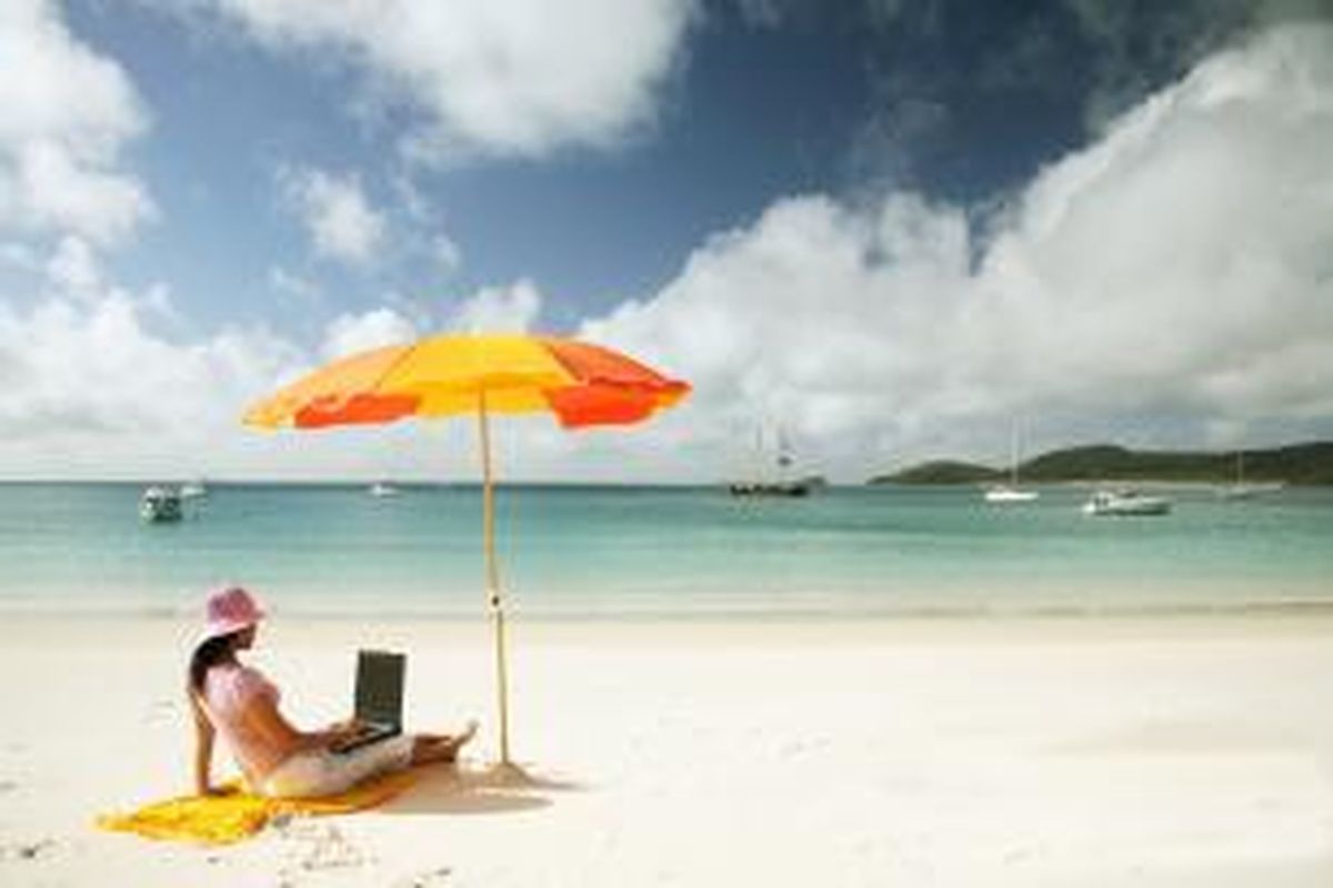 ILUSTRASI - Turis tengah menggunakan laptop saat berwisata di pantai. 
