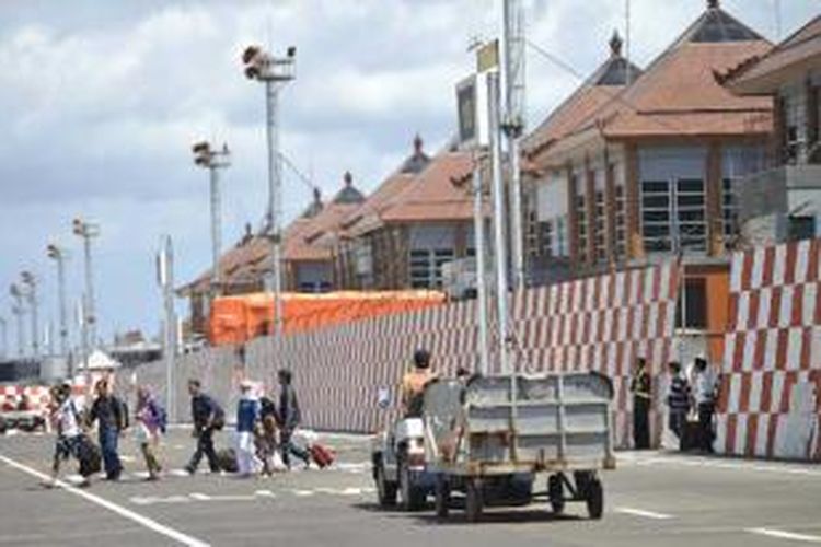 Para penumpang pesawat melintasi pagar yang dibangun selama proses renovasi perluasan Bandara Internasional Ngurai Rai Bali, Kamis (22/8/2013). Proyek tersebut diharapkan bisa selesai sebelum Konferensi Tingkat Tinggi (KTT) Asia-Pasific Economic Cooperation (APEC) yang akan berlangsung pada awal Oktober mendatang.