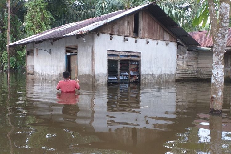 Seorang warga mengarungi banjir untuk pergi ke rumahnya di Desa Padang Luas, Kecamatan Tambang, Kabupaten Kampar, Riau, Senin (16/12/2019).