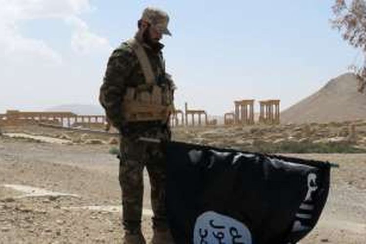 Seorang prajurit Suriah membawa bendera hitam ISIS yang diturunkan setelah merebut kembali kota Palmyra, Minggu (27/3/2016).