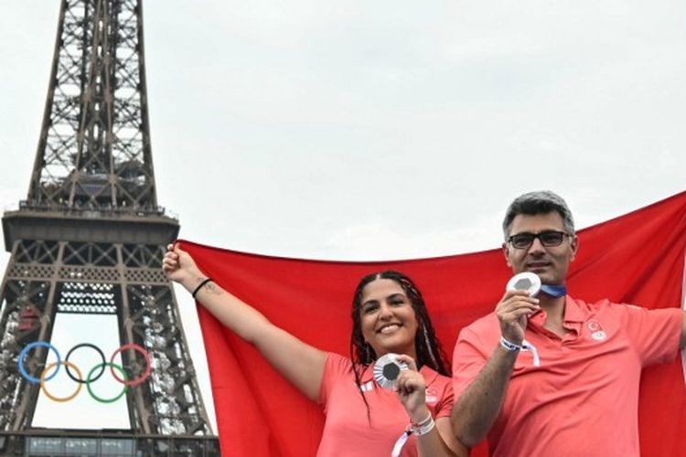 Sevval Ilayda Tarhan dan Yusuf Dikec berpose di Champions Park di depan Menara Eiffel pada Kamis (31/7/2024) setelah meraih medali perak cabor menembak. Yusuf Dikec viral di media sosial karena menembak tanpa menggunakan peralatan khusus. (Photo by Miguel MEDINA / AFP)