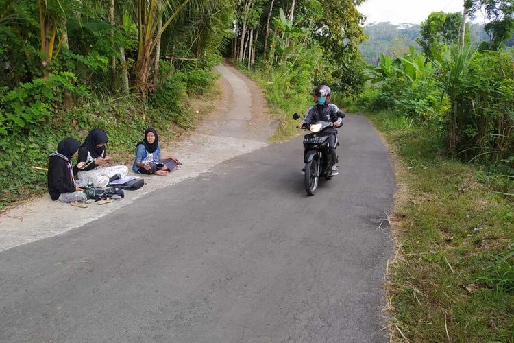 Teara, adik dan kawannya mengikuti kuliah daring di tepi jalan karena sulit sinyal internet, di Desa Kenalan, Kecamatan Borobudur, Kabupaten Magelang.