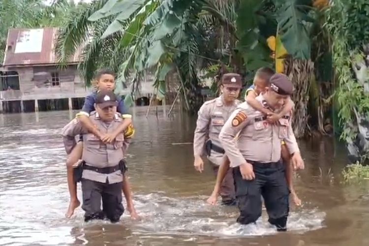 Petugas kepolisian menggendong anak-anak yang terjebak banjir di Kepenghuluan Sei Kapas, Kecamatan Rantau Kopar, Kabupaten Rokan Hilir, Riau, Kamis (7/12/2023).