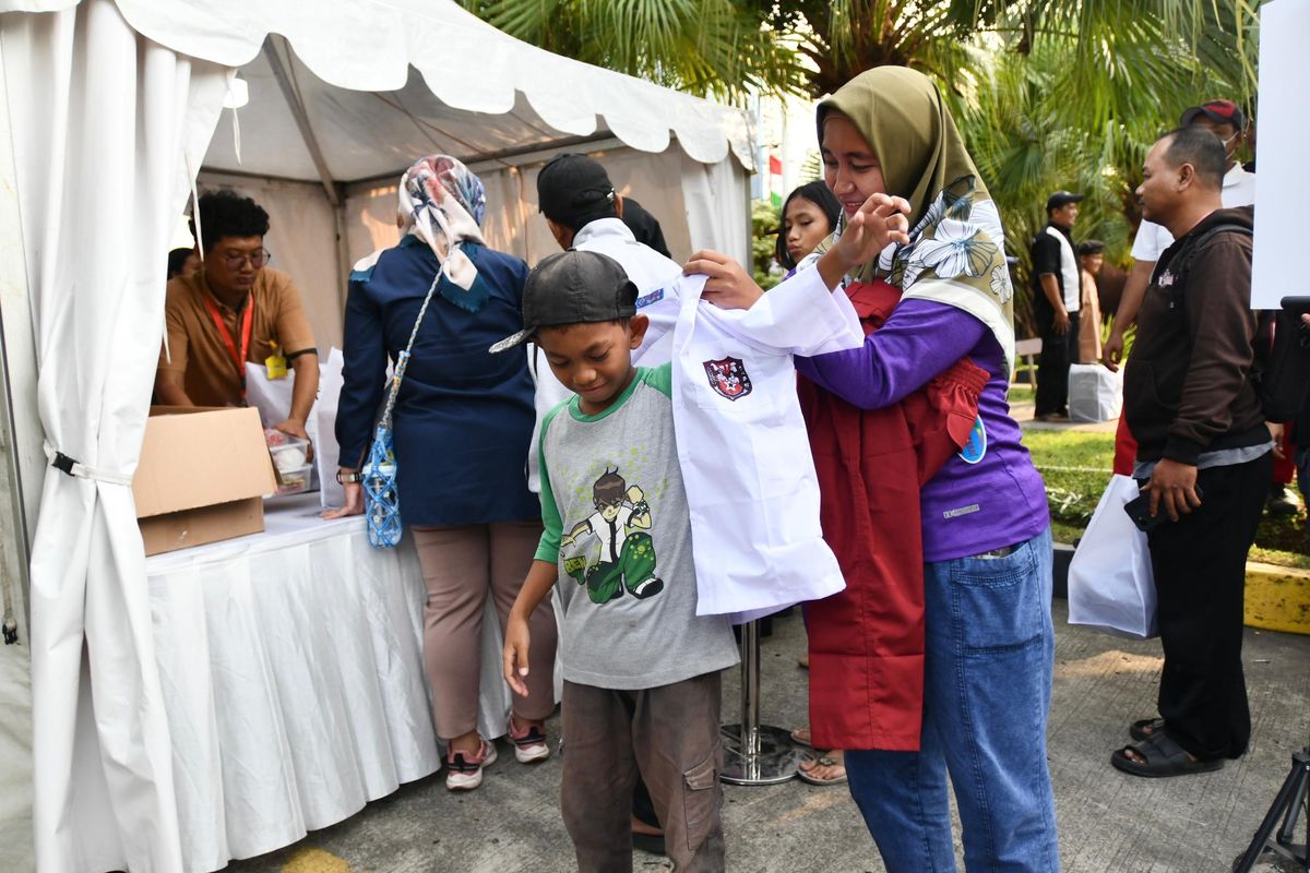 Orangtua penerima manfaat program Seribu Seragam Sekolah Bersama Pertamina (SESAMA) dari PT Pertamina (Persero) sedang mengenakan seragam sekolah merah putih kepada anaknya.