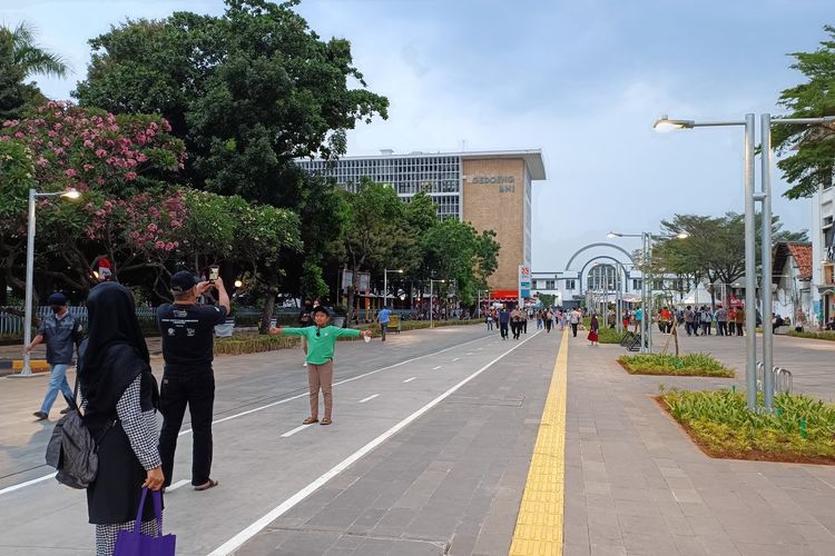 Warga berfoto di Jalan Lada dengan latar Gedung BNI dan Stasiun Jakarta Kota, Jumat (26/08/2022). Sebagai bagian dari revitalisasi kawasan Kota Tua, Jalan Lada turut diubah menjadi area pejalan kaki.