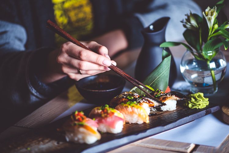 Ilustrasi orang makan sushi menggunakan sumpit. 
