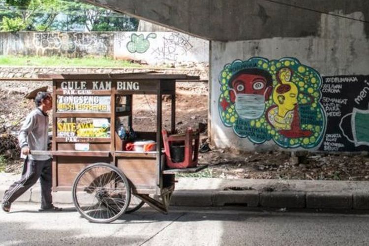 Pedagang kaki lima berjalan di dekat mural bertema pencegahaan penyebaran virus Corona atau COVID-19 di Jakarta, Rabu (01/04) 