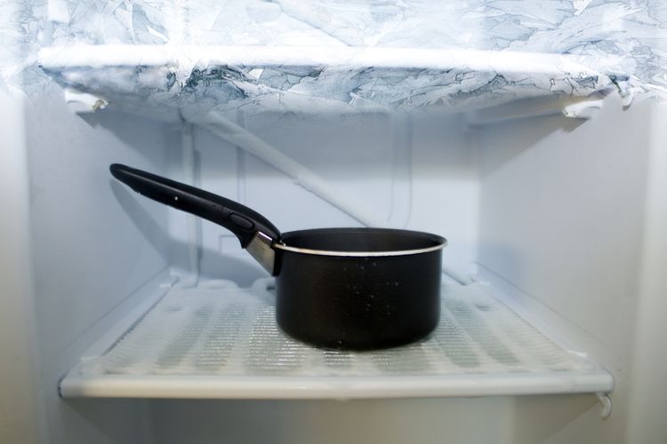 Ilustrasi membersihkan bunga es freezer menggunakan panci berisi air panas. 