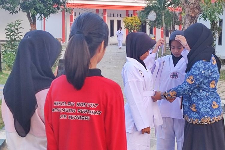Husna, siswi Sekolah Rakyat Menengah Pertama saat dikenakan sabuk baju Taekwondo oleh wali asuhnya di depan dekat Asrama mereka.