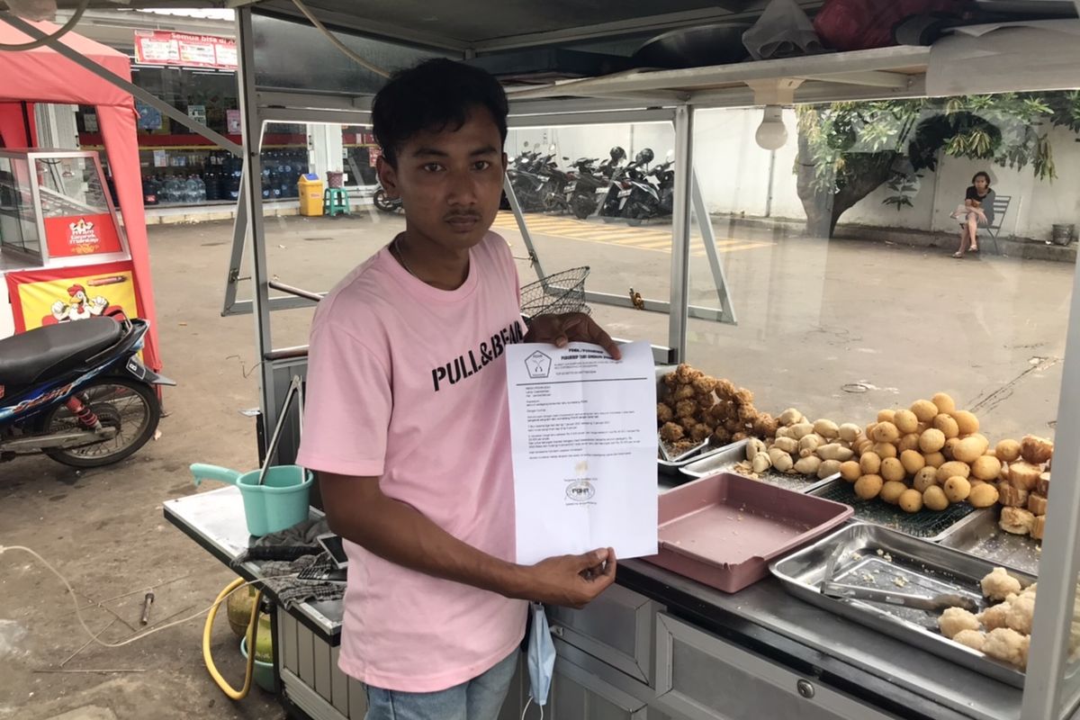 Acep (20), pedagang gorengan di Jalan Taman Margasatwa Ragunan menunjukkan surat pemberitahuan pabrik tahu dan tempe yang mogok produksi di tempatnya berjualan pada Minggu (3/1/2021) siang.