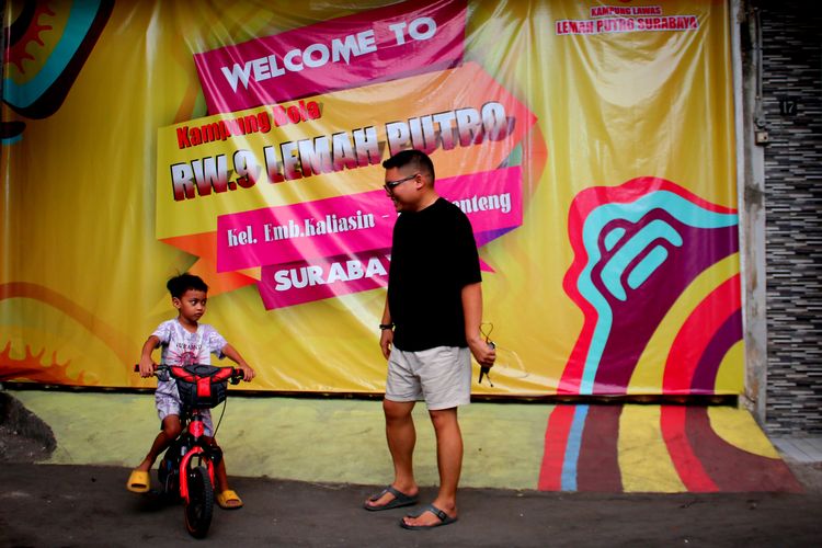 Seorang warga sedang ngobrol didepan banner untuk menyemarakan Piala Dunia U17 2023 Indonesia yang ada di Kampung Lemah Putro Jalan Embong Kaliasin Gang III dan IV, Kota Surabaya, Jawa Timur.