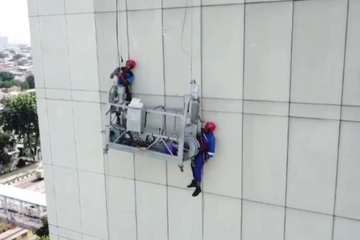 Dua pekerja yang sedang membersihkan gedung tersangkut di gondola gedung UNJ, Jakarta Timur, Jumat (2/2/2024). 