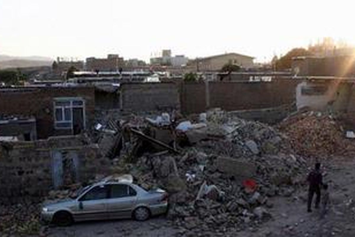 Seorang pria Iran dan seorang anak berjalan melewati rumah yang hancur di kota Varzaqan sekitar 60 km timur laut kota Tabriz setelah gempa bumi kembar menghantam barat laut Iran pada 11 Agustus 2012. 