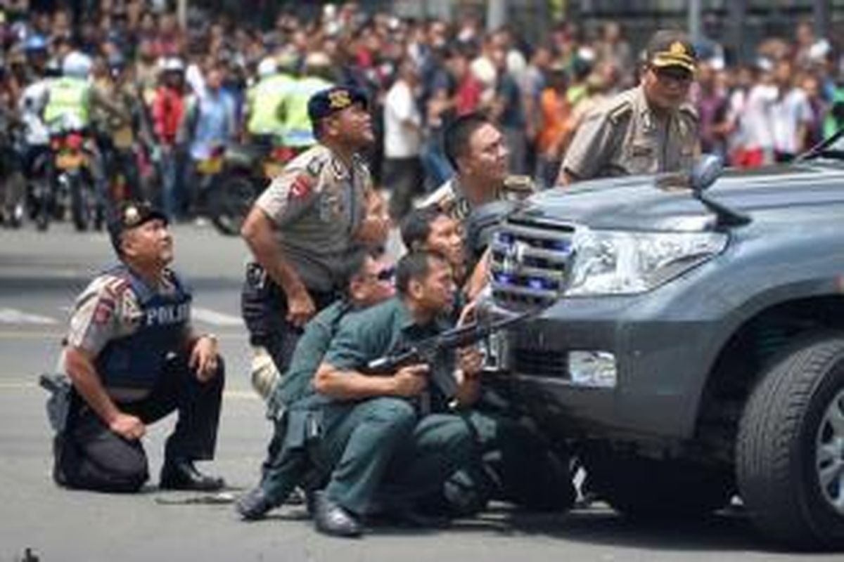 Polisi berlindung di balik kendaraan saat mengejar terduga pelaku setelah ledakan menghantam kawasan Jalan MH Thamrin, Jakarta Pusat, 14 Januari 2016. Serangkaian ledakan menewaskan sejumlah orang, terjadi baku tembak antara polisi dan beberapa orang yang diduga pelaku.