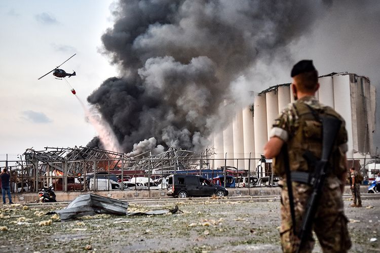 Petugas berjaga saat helikopter memadamkan api di lokasi ledakan di kawasan pelabuhan di Beirut, Ibu Kota Lebanon, Selasa (4/8/2020). Sebanyak 73 orang tewas dan ribuan lainnya dilaporkan terluka dari insiden dua ledakan besar yang mengguncang Beirut tersebut.