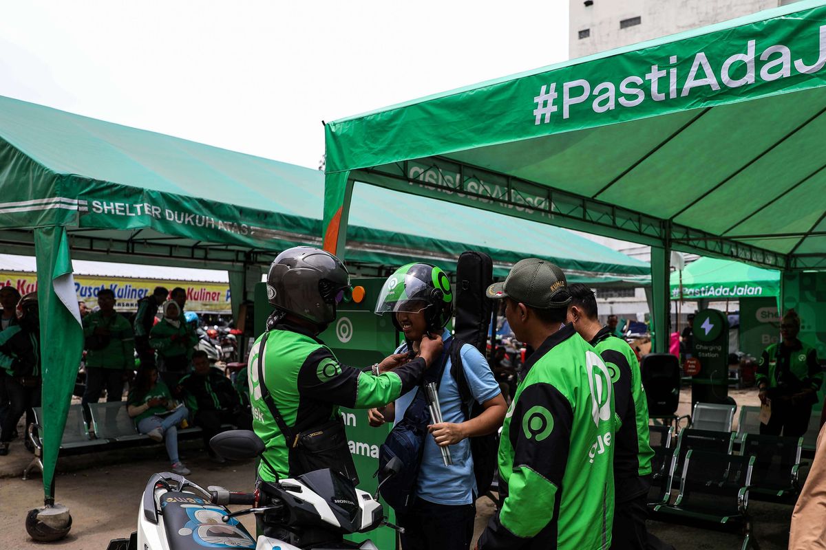 Pengemudi ojek online memakaikan helm kepada penumpangnya di Kawasan Stasiun Sudirman, Jakarat Pusat, Rabu (11/3/2020). Kenaikan tarif ojek online batal diterapkan 14 Agustus 2022.