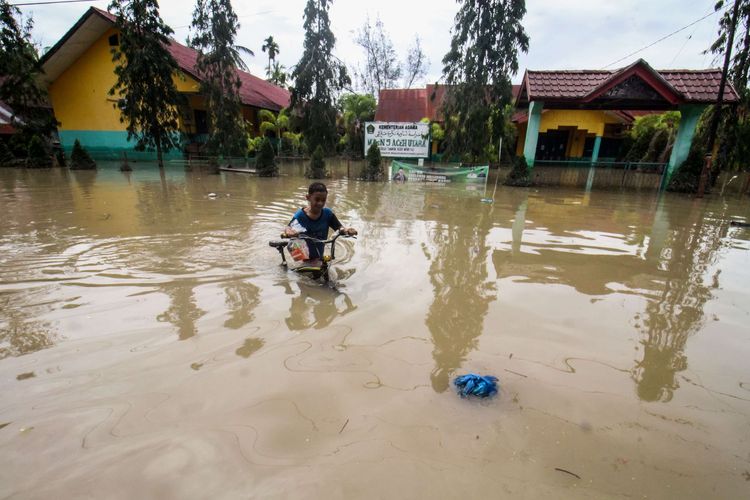 Seorang anak menuntut sepedanya di tengah banjir yang melanda Kecamatan Matang Kuli, Aceh Utara, Aceh, Senin (23/1/2023). Menurut Badan Penanggulangan Bencana Daerah (BPBD) Aceh Utara, hujan deras yang mengguyur Aceh Utara dalam dua hari terakhir mengakibatkan tujuh kecamatan di Aceh Utara terendam banjir dan sebanyak 11.202 jiwa warga terdampak banjir serta 420 jiwa mengungsi.