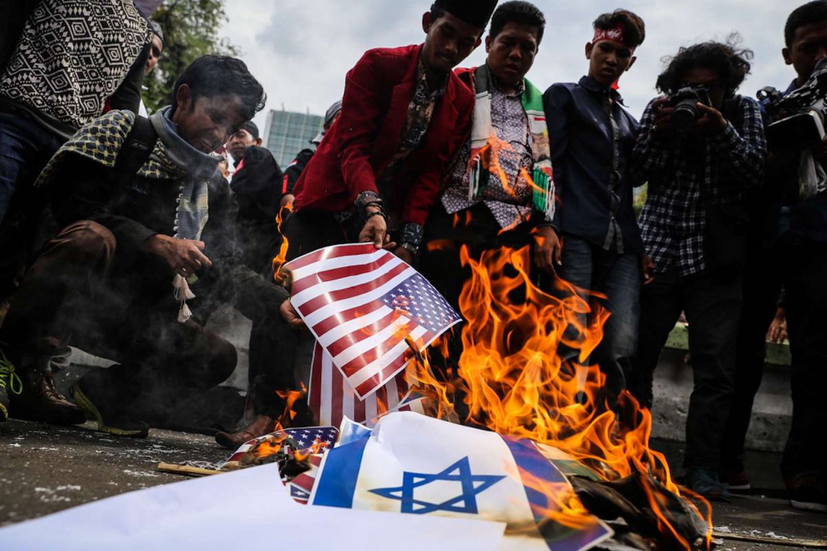 Massa membakar foto bendera Israel dan Amerika Serikat saat aksi unjuk rasa untuk Palestina di depan Kedubes Amerika Serikat, Jalan Medan Merdeka Selatan, Jumat (15/12/2017). Aksi bela Palestina ini dilakukan untuk merespons keputusan Presiden AS Donald Trump dalam menetapkan Jerusalem sebagai Ibu Kota Israel.