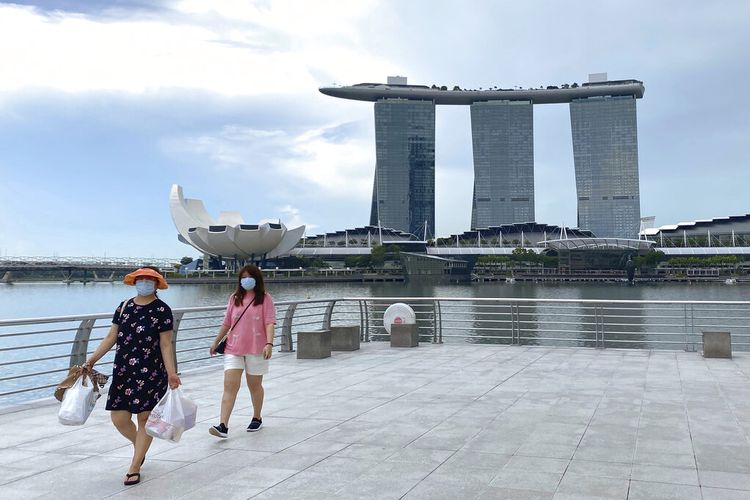 Pengunjung memakai masker saat berjalan di sekitar Merlion Park, tujuan wisata populer, dengan latar belakang Marina Bay Sands di Singapura Senin, 31 Mei 2021. 
