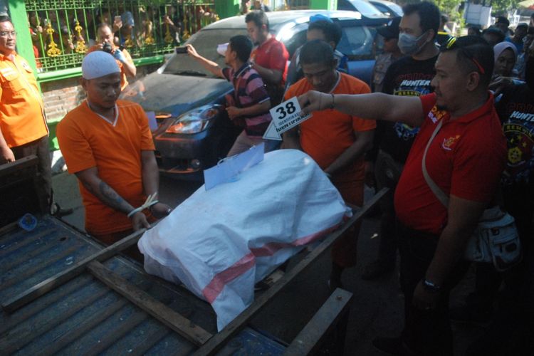 Reka ulang atas kasus pembunuhan terhadap pria berkaos Polisi yang ditemukan terbakar di sebuah ladang tanaman kayu putih, di Mojokerto, Selasa (25/6/2019). Pada adegan ke 38, tubuh korban yang dibungkus karung plastik, dinaikkan ke mobil pickup oleh pelaku pembunuhan.