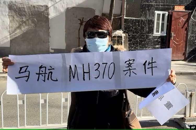 Hu Xiufang, yang putra, menantu, dan cucunya termasuk dalam pesawat MH370 yang hilang, memegang spanduk di Beijing Senin, 27 November 2023.