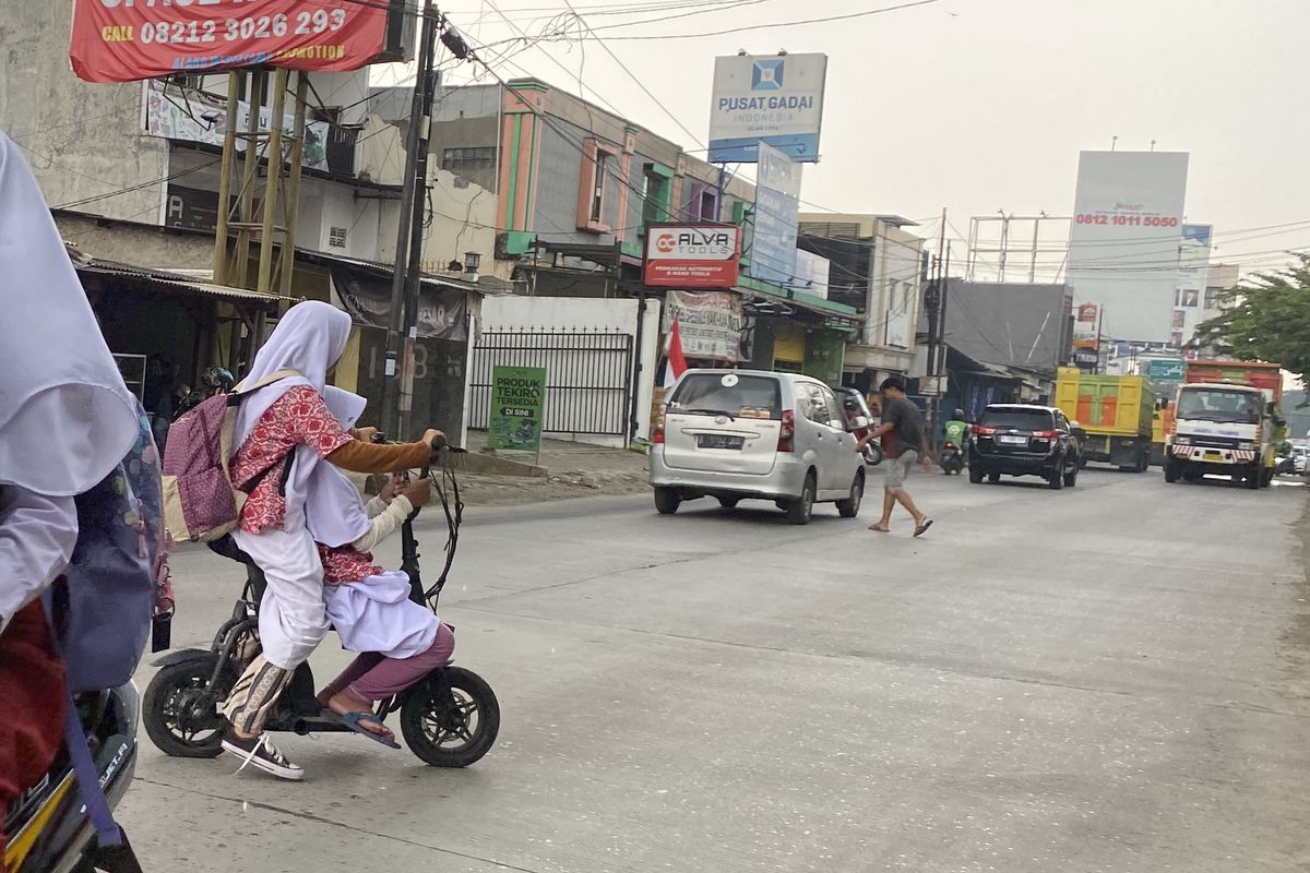 Potret anak kecil menggunakan sepeda listrik di jalan umum, penuh mobil, truk dan motor yang lalu-lalang