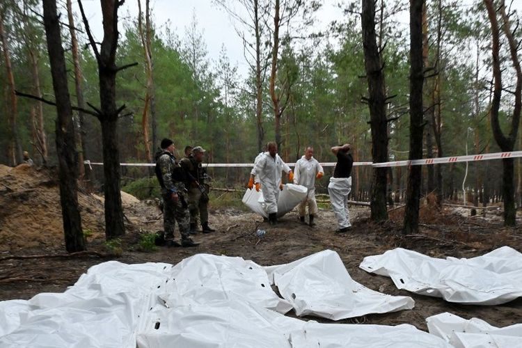 Petugas forensik membawa kantong mayat di hutan pinggiran Izyum, Ukraina timur, 16 September 2022.
