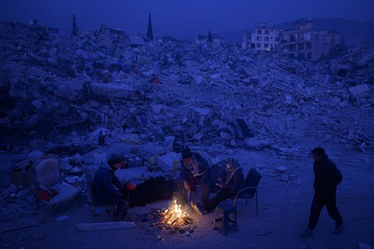 Penduduk setempat menunggu kabar dari kerabat mereka, duduk di dekat api unggun di antara puing-puing bangunan yang runtuh di Hatay, Turkiye pada Selasa (14/2/2023), setelah gempa berkekuatan magnitudo 7,8 melanda tenggara negara itu. Pada Jumat (17/2/2023), tujuh orang sekeluarga asal Suriah dilaporkan meninggal dunia akibat kebakaran di Turkiye pada Jumat (17/2/2023).