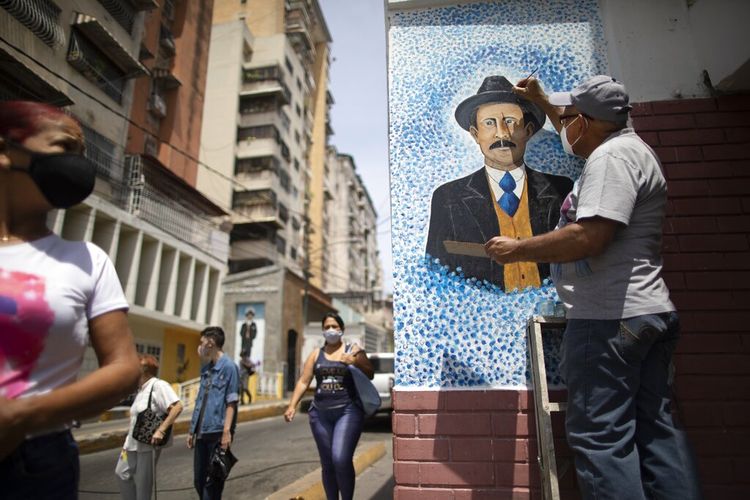 Seniman Mervin Marmol memberikan sentuhan akhir pada lukisan mendiang Dr Jose Gregorio Hernandez di sudut jalan tempat ia meninggal dalam kecelakaan mobil pada 1919 di lingkungan La Pastora di Caracas, Venezuela, Senin (26/4/2021).