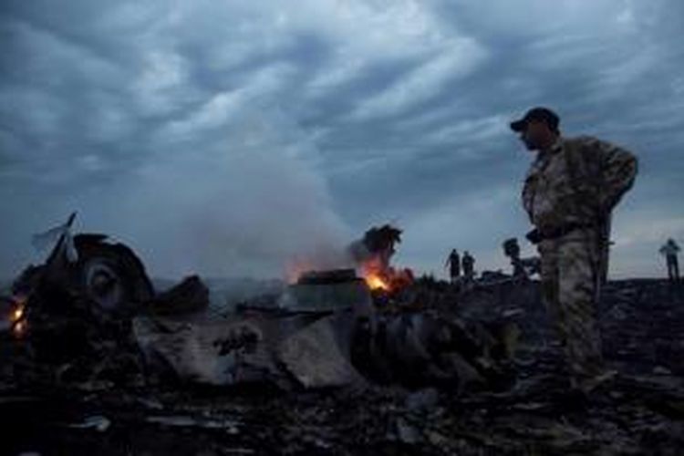 Seorang pria mengenakan seragam militer berada di dekat puing pesawat Malaysia Airlines yang membawa 295 orang penumpang dari Amsterdam ke Kuala Lumpur yang jatuh di Desa grabovo, Shaktarsk, timur Ukraina, Kamis (17/8/2014).