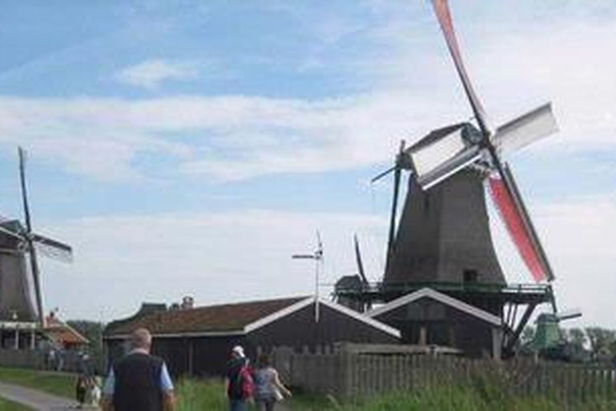 wisatawan menyusuri jalanan dengan latar belakang kincir angin