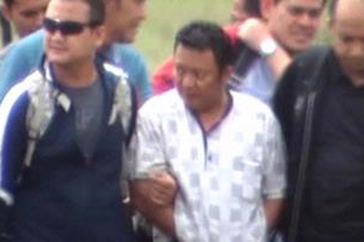 Bupati Buol Amran Batalipu saat digiring turun dari pesawat yang membawanya ke Bandara Mutiara, Palu, Jumat siang