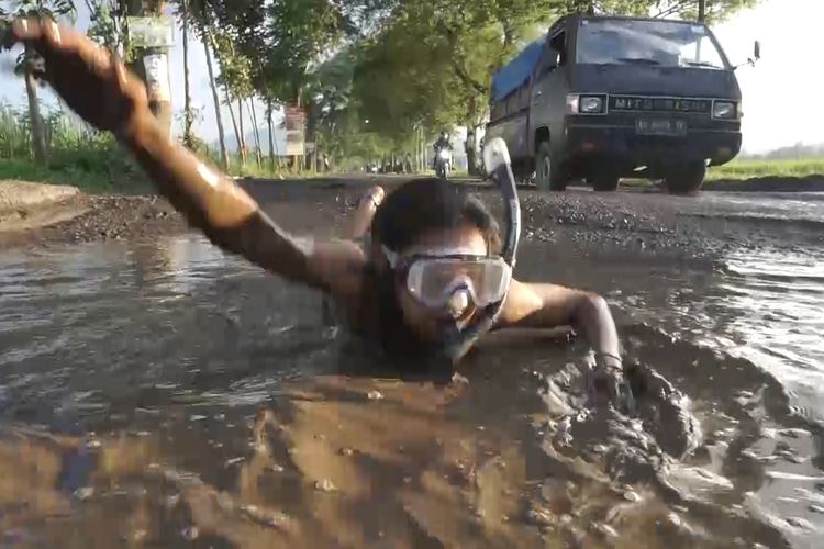 Salah satu pelaku seni Trenggalek, melakukan aksi berenang di lubang jalan yang rusak, yang berada di Kec. Karangan Trenggalek, Jawa Timur.