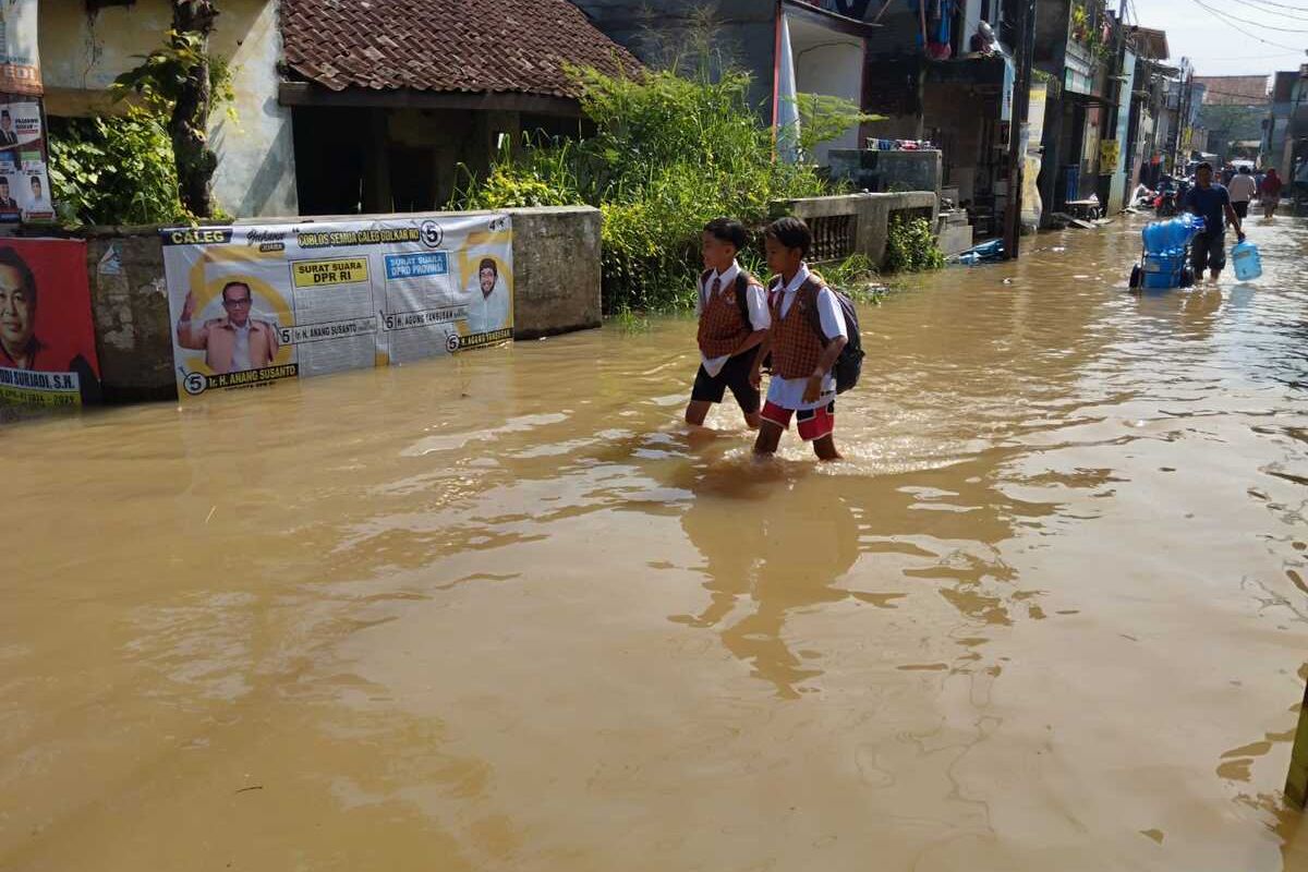 Dua orang anak Sekolah Dasar Negeri (SDN) Zipur 5 saat melewati banjir di Kampung Bojongasih, Desa Dayeuhkolot, Kecamatan Dayeuhkolot, Kabupaten Bandung, Jawa Barat saat akan berangkat sekolah pada hari pertama sekolah Senin (8/1/2024)